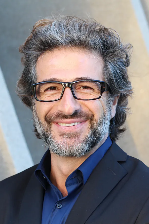 A man with glasses, salt and pepper hair and a beard smiling because he received treatment for andropause and low testosterone from Dr. Hadi Michael Rassael at Millennium Wellness in Bethesda-Chevy Chase.