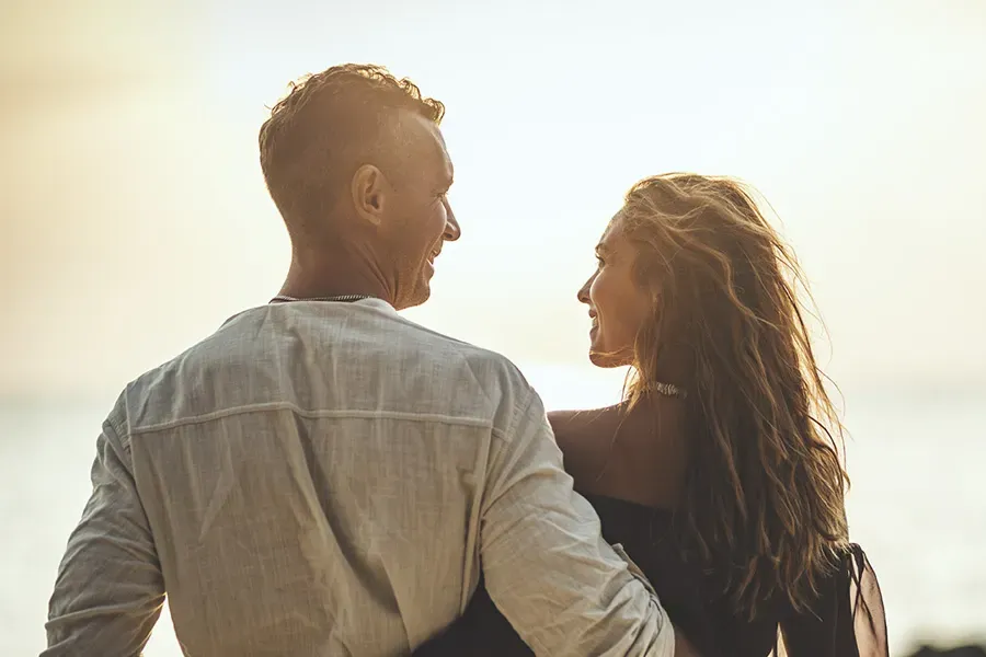 A couple gazes at each other on the beach at sunrise, viewed from behind. Schedule Anti-Aging treatment from Dr. Hadi Michael Rassael at Millennium Wellness in Bethesda-Chevy Chase.