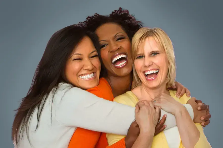 Three joyful women embracing in a group hug, laughing and smiling after receiving Bioidentical Hormone Pellet Therapy by Dr. Hadi Michael Rassael at Millennium Wellness in Bethesda-Chevy Chase.