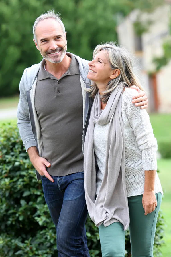 A mature couple in gray toned clothes and jeans walk happily outside, happy with their successful bioidentical hormone treatments from Dr. Hadi Michael Rassael at Millennium Wellness in Bethesda-Chevy Chase.
