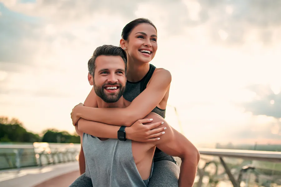 A fit couple embrace on a bridge after a run. Schedule body contouring and sculpting treatments from Dr. Hadi Michael Rassael at Millennium Wellness in Bethesda-Chevy Chase.