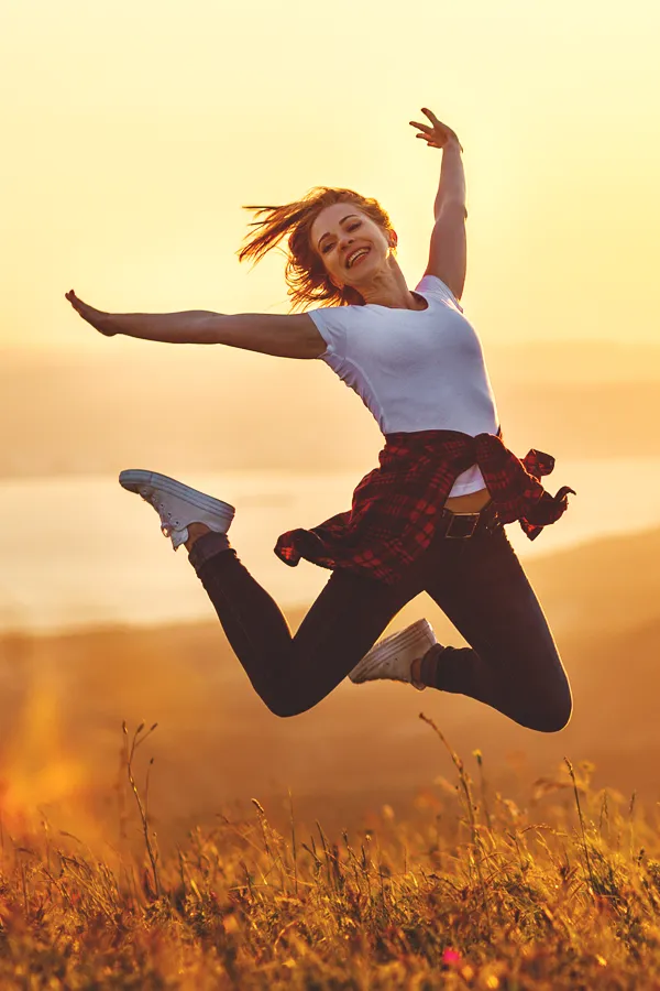 A woman jumps for joy in a field at sunset. Get breast augmentation treatment from Dr. Hadi Michael Rassael at Millennium Wellness in Bethesda-Chevy Chase.