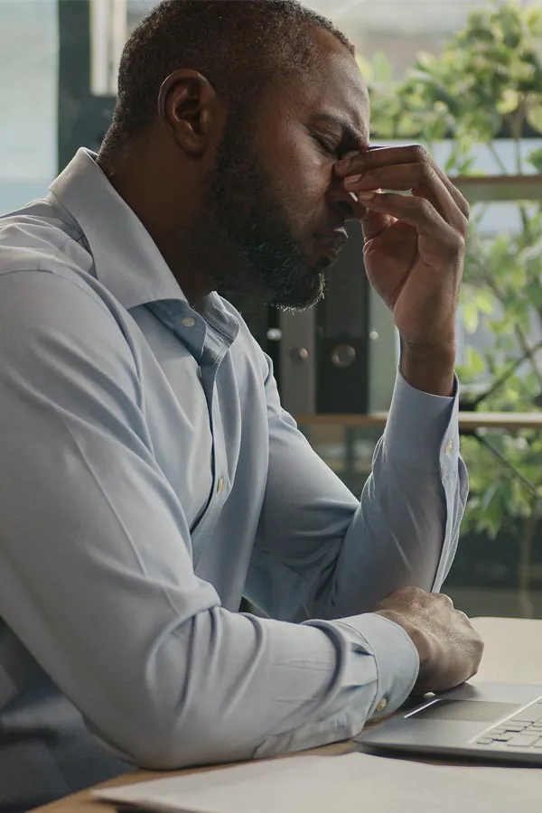 A black man rubbing the top of his nose at his desk, in need of chronic fatigue treatment from Dr. Hadi Michael Rassael at Millennium Wellness in Bethesda-Chevy Chase.