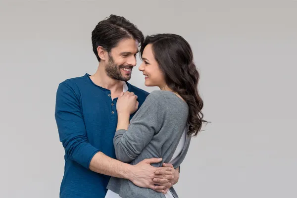 A man in a blue shirt embracing a woman in a gray shirt smiles due to his successful erectile dysfunction care from Dr. Hadi Michael Rassael at Millennium Wellness in Bethesda-Chevy Chase.