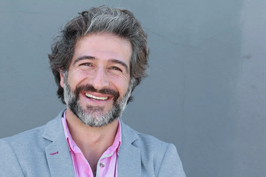 A smiling middle-aged man with a full, even beard. Get facial hair transplant treatment from Dr. Hadi Michael Rassael at Millennium Wellness in Bethesda-Chevy Chase.