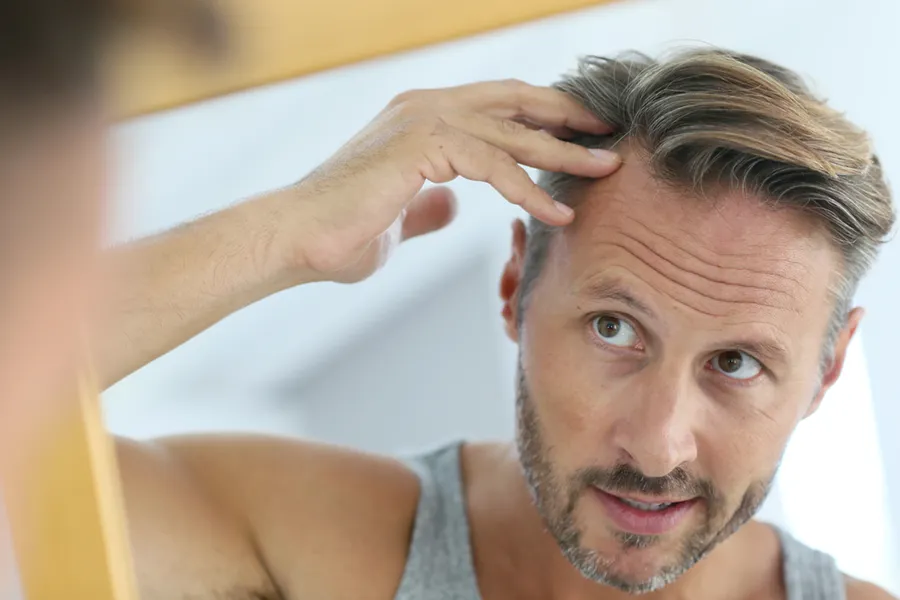 A middle-aged man looks in the mirror, worried about his hairline. Schedule hair restoration treatments from Dr. Hadi Michael Rassael at Millennium Wellness in Bethesda-Chevy Chase.