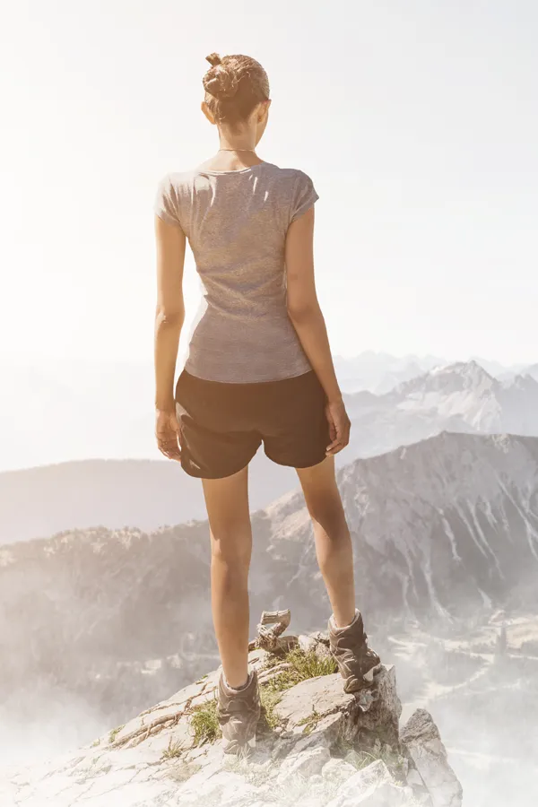 A woman in athletic clothes stands triumphantly on a mountaintop. Get joint pain treatment from Dr. Hadi Michael Rassael at Millennium Wellness in Bethesda-Chevy Chase.
