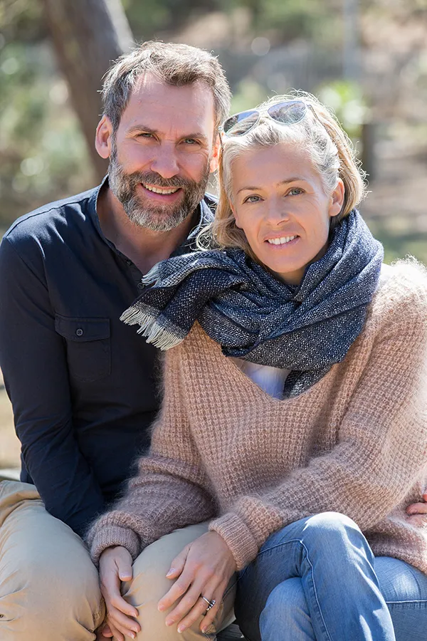 A middle-aged couple with youthful skin sit outside on a cold day. Get laser skin tightening treatment from Dr. Hadi Michael Rassael at Millennium Wellness in Bethesda-Chevy Chase.