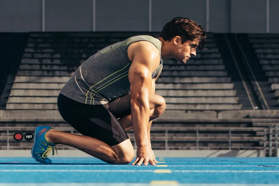 A white man kneels at the starting line on a track, determined to do his best. Get treatment for lean muscle loss and recovery from Dr. Hadi Michael Rassael at Millennium Wellness in Bethesda-Chevy Chase.