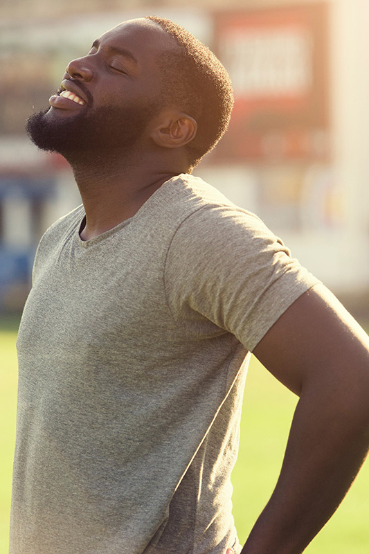 A black man in a gray t-shirt and smiles, looking up with closed eyes after a satisfying workout. Get treatment for lean muscle loss and recovery from Dr. Hadi Michael Rassael at Millennium Wellness in Bethesda-Chevy Chase.