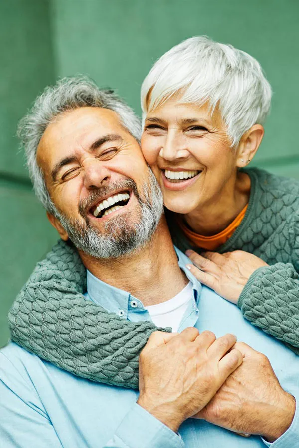 An trim older couple embracing and smiling on their porch. Get liposuction treatment from Dr. Hadi Michael Rassael at Millennium Wellness in Bethesda-Chevy Chase.