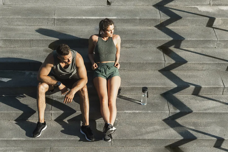 A couple in gray and green track clothes resting after a workout on stone steps, happy with their weight loss plans from Dr. Hadi Michael Rassael at Millennium Wellness in Bethesda-Chevy Chase.
