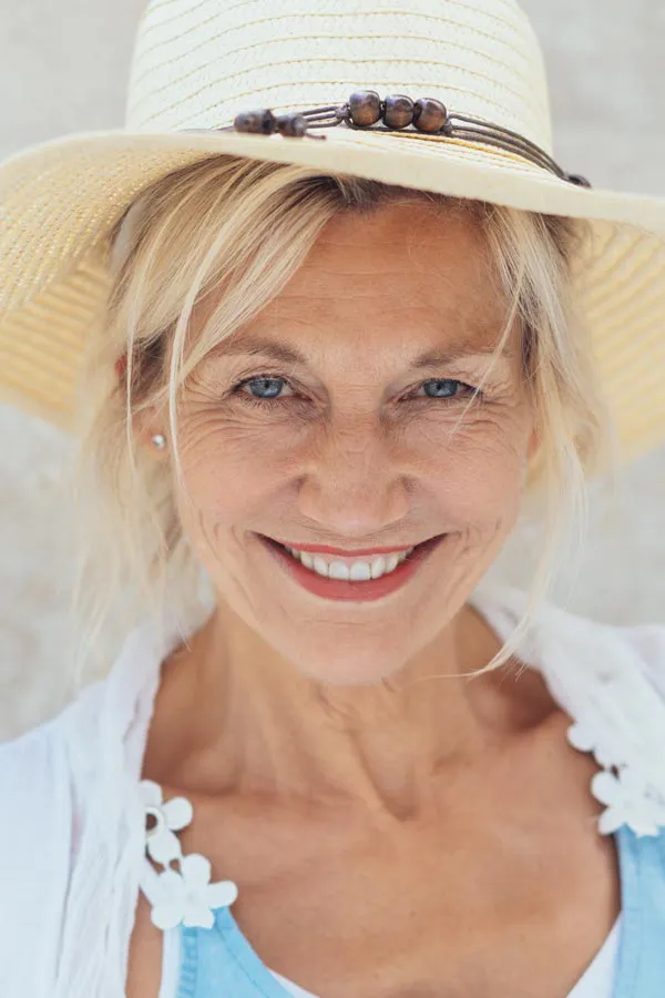 A beautiful, smiling older woman with blonde hair and a sunhat, happy with menopause treatment from Dr. Hadi Michael Rassael at Millennium Wellness in Bethesda-Chevy Chase.
