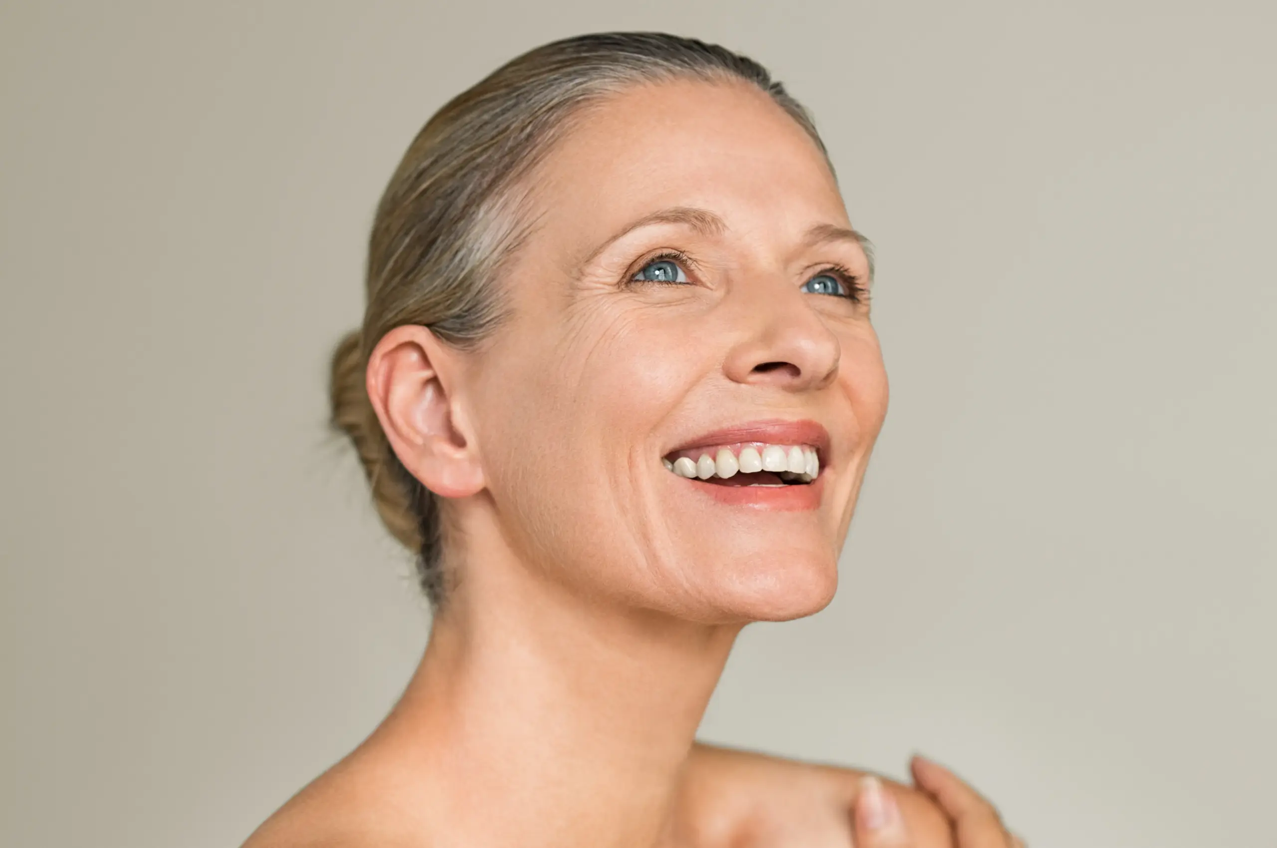A mature woman with a youthful neck smiles and looks up. Get a neck lift from Dr. Hadi Michael Rassael at Millennium Wellness in Bethesda-Chevy Chase.
