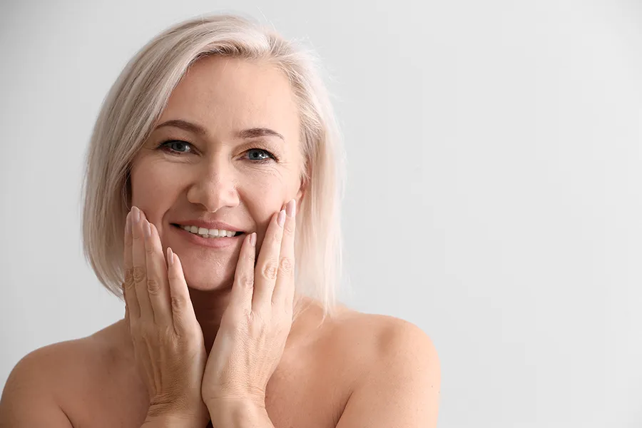 A mature woman touches her faces to feel the successful results of PRP microneedling and skin rejuvenation treatments from Dr. Hadi Michael Rassael at Millennium Wellness in Bethesda-Chevy Chase.