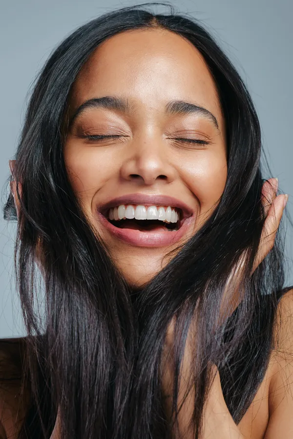 A beautiful latin woman smiles and runs her fingers through her long, beautiful hair, happy with her PRP for hair loss and restoration treatment from Dr. Hadi Michael Rassael at Millennium Wellness in Bethesda-Chevy Chase.