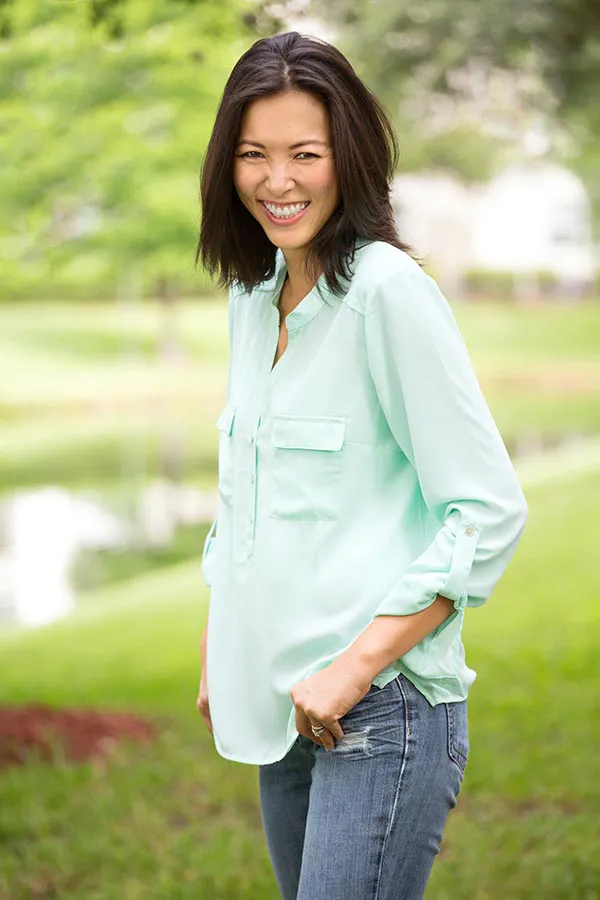 A middle-aged brunette woman in a light green button-up shirt stands outside smiling, happy with her perimenopause treatment from Dr. Hadi Michael Rassael at Millennium Wellness in Bethesda-Chevy Chase.