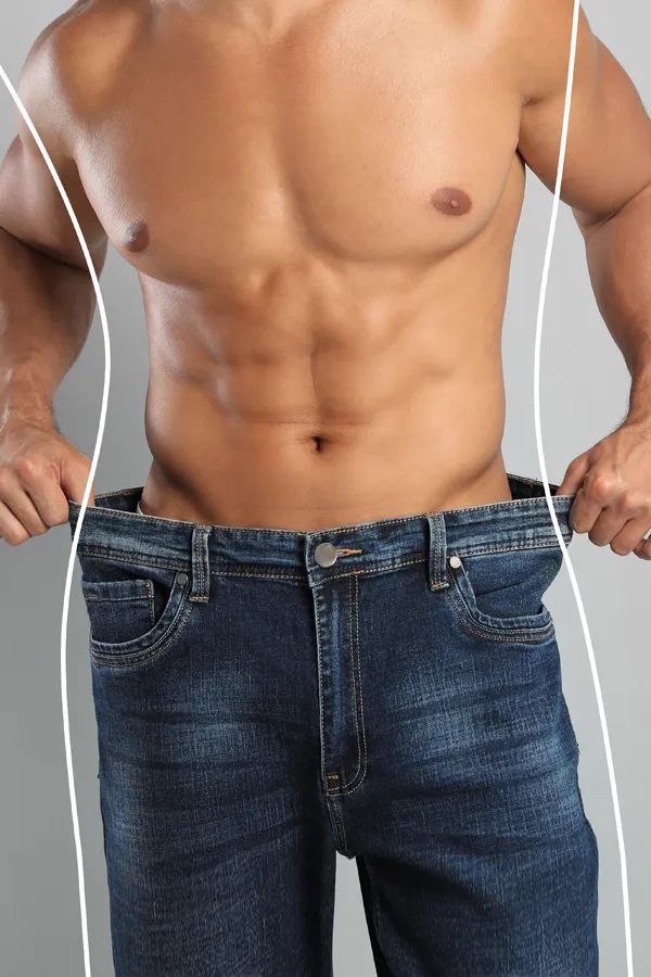 A strong shirtless man in jeans holds the waistlines of his too-big jeans to show the success of semaglutide weight loss from Dr. Hadi Michael Rassael at Millennium Wellness in Bethesda-Chevy Chase.
