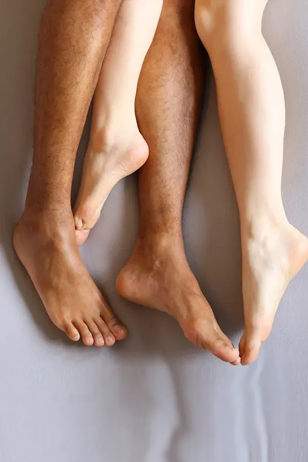 Photo from the knees to the feet of a couples nude legs entwined on a bed, representing shockwave treatment for erectile dysfunction from Dr. Hadi Michael Rassael at Millennium Wellness in Bethesda-Chevy Chase.