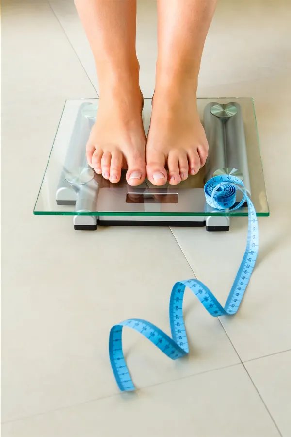 Close-up of a woman's feet standing on a scale, with measuring tape by her toes, getting treatment for weight loss resistance from Dr. Hadi Michael Rassael at Millennium Wellness in Bethesda-Chevy Chase.